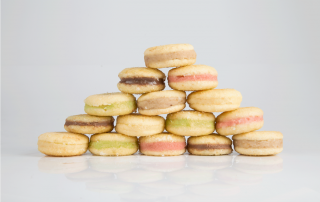 A imagem apresenta 15 unidades de bem casado da Zulmira Doces de diferentes sabores: tradicional de doce de leite, pistache, nozes, frutas vermelhas e chocolate que estão empilhados em formato de pirâmide